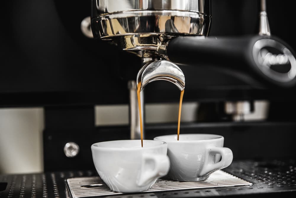 Baristakurs-Kompakt Espresso läuft aus einem bodenlosen Siebträger in zwei weiße Tassen