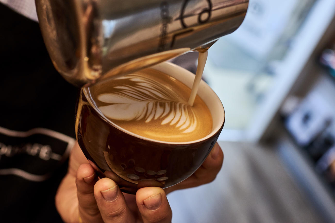 Kaffee und Barista Erlebnisseminar Barista gießt Latte Art in eine Cappuccinotasse