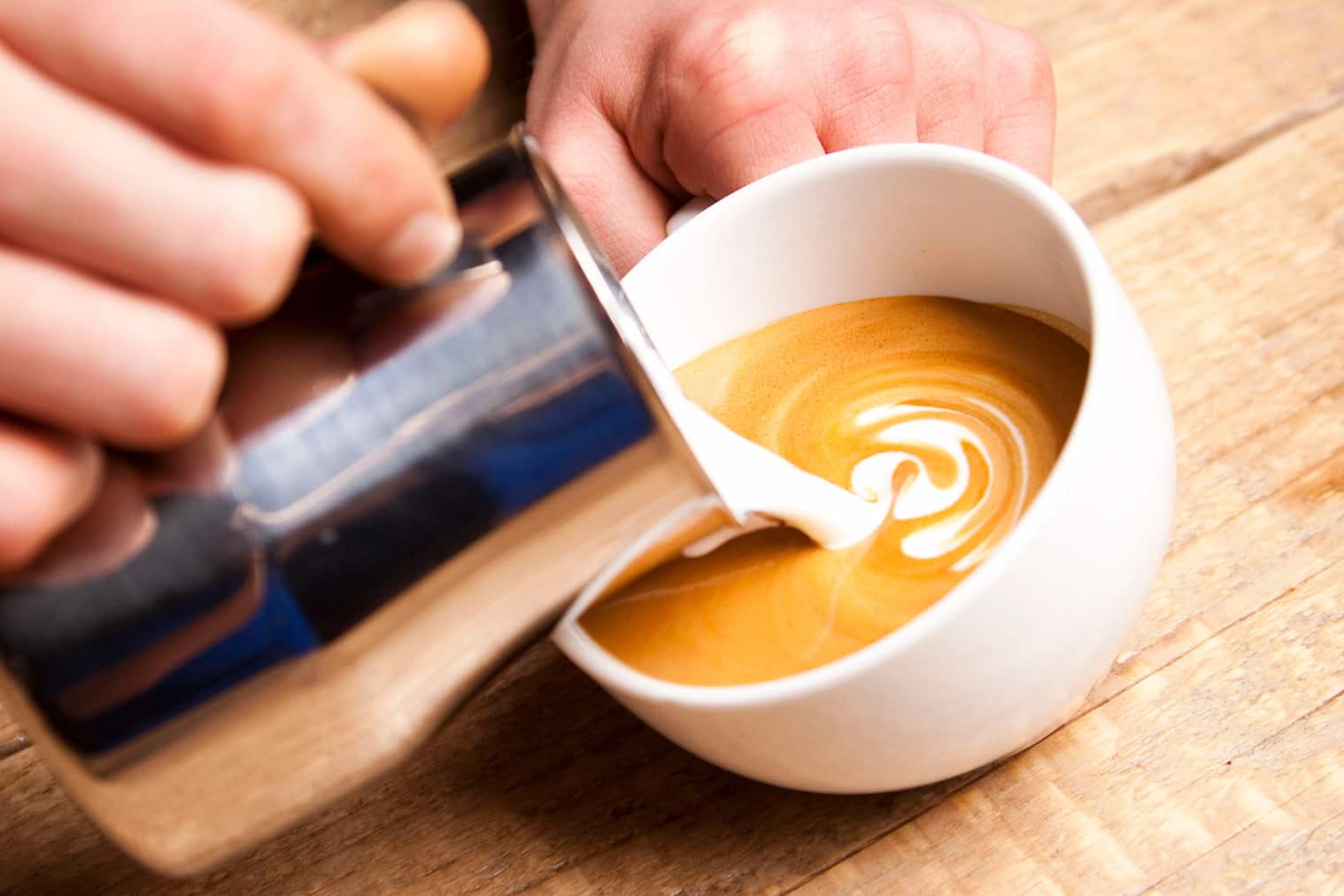 Latte Art Kurs Basic Barista gießt Milchschaum in eine Tasse mit Espresso